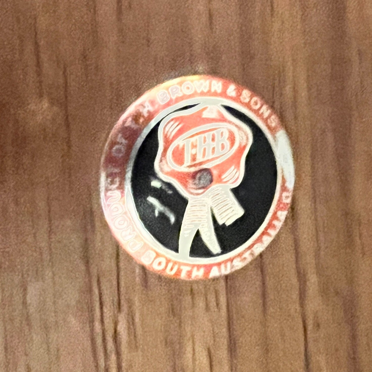 THBrown Round sticker with a logo on a wooden surface
